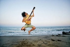 Umelecká fotografie Mixed Race man playing guitar and jumping at beach, Peathegee Inc, (40 x 26.7 cm)